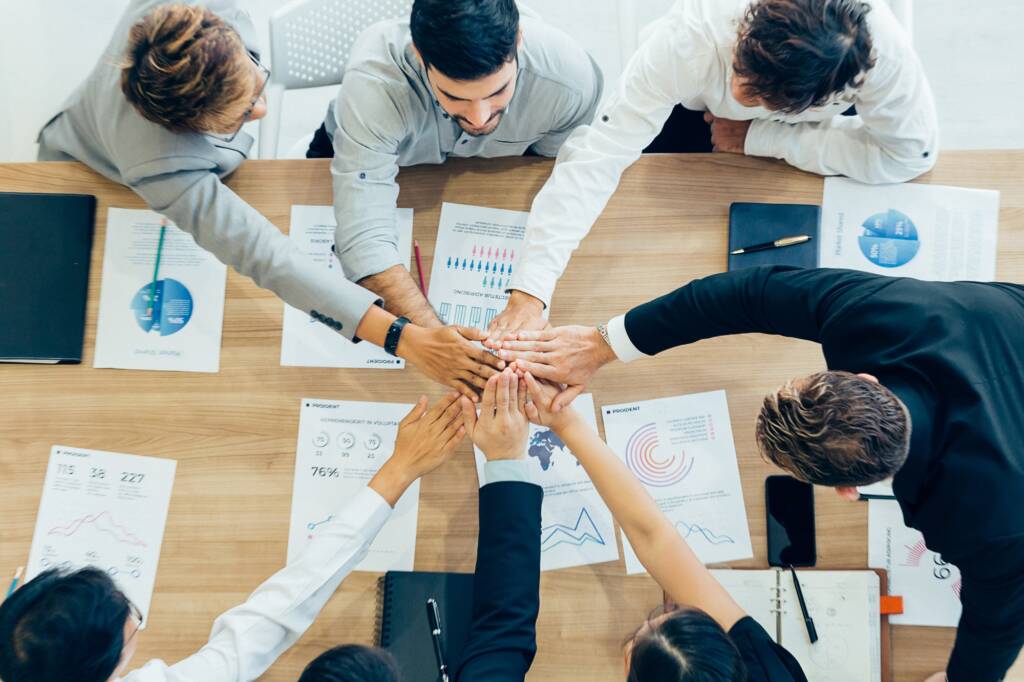Colleagues stacking hands above table with papers